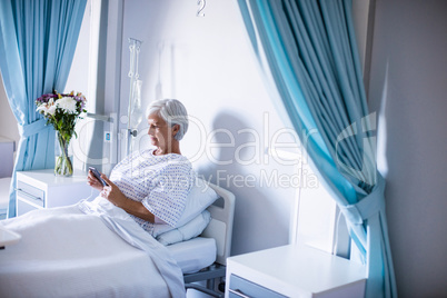 Female senior patient using mobile phone on bed