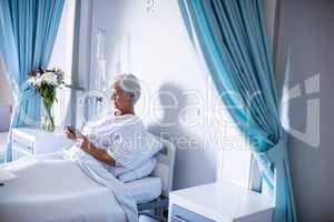 Female senior patient using mobile phone on bed