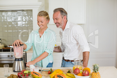 Smiling couple preparing fresh juice in kitchen