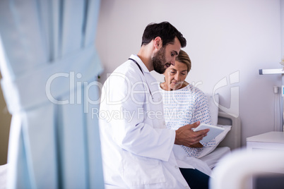 Male doctor showing digital tablet to female senior patient in the ward