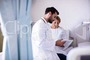 Male doctor showing digital tablet to female senior patient in the ward