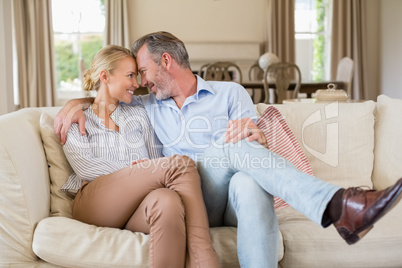 Romantic couple sitting on sofa with arm around in living room