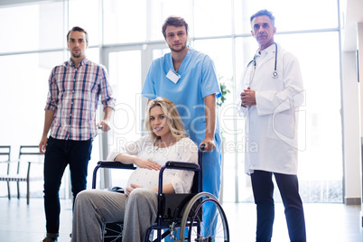 Portrait of smiling doctor carrying pregnant woman in a wheelchair