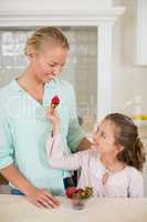 Daughter giving strawberry to mother in kitchen