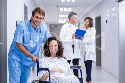 Portrait of doctor pushing a pregnant woman on wheelchair