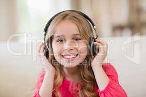 Smiling cute girl listening to music on headphones in living room at home