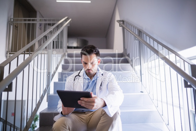 Doctor sitting on staircase using digital tablet