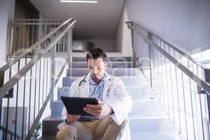 Doctor sitting on staircase using digital tablet