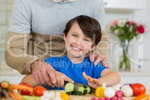 Father and son slicing a cucumber on chopping board in kitchen