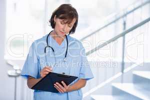 Smiling doctor writing on clipboard in corridor