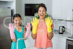Portrait of daughter and mother showing gloves in kitchen