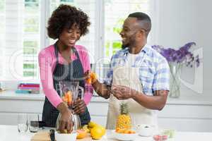 Smiling couple preparing fruit juice in kitchen
