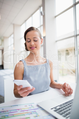 Businesswoman sitting with laptop and using mobile phone