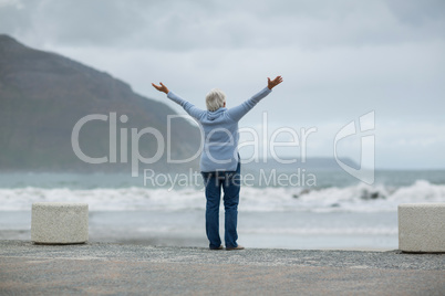 Senior woman standing with arms outstretched on the beach