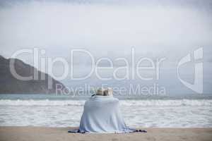 Mature couple wrapped in blanket on the beach