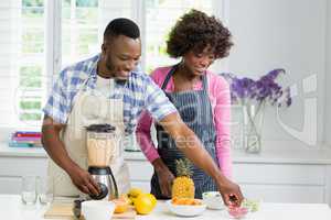 Smiling couple preparing fruit juice in kitchen