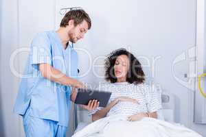 Doctor assisting pregnant woman on digital tablet in ward