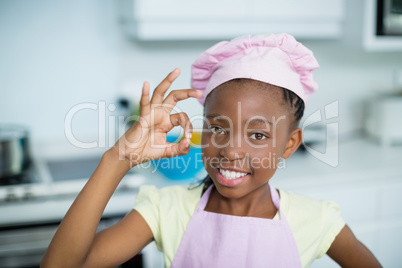 Portrait of girl showing hand ok sign in kitchen