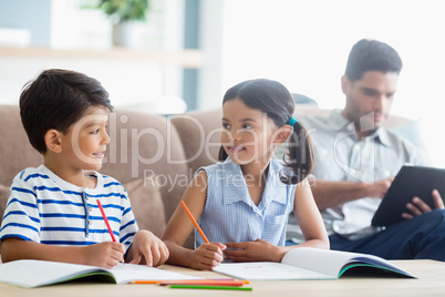 Smiling siblings doing homework in living room