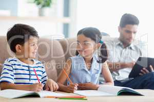 Smiling siblings doing homework in living room