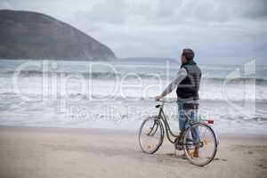 Mature man standing with bicycle on the beach