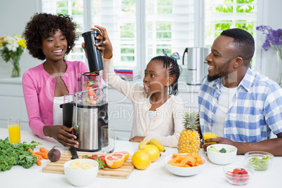 Smiling parents and daughter preparing strawberry smoothie in kitchen