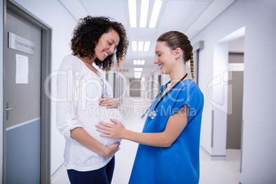 Doctor touching pregnant womans belly in corridor