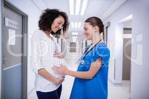 Doctor touching pregnant womans belly in corridor