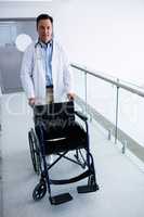 Male doctor pushing an empty wheelchair in the passageway