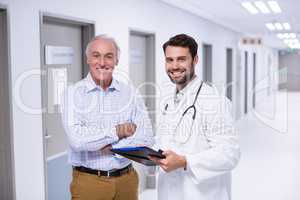 Portrait of doctor and patient discussing on clipboard in corridor