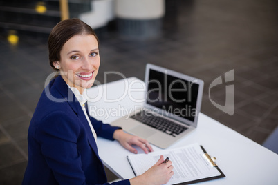 Businesswoman sitting at desk with clipboard and laptop