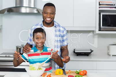 Father and son preparing salad in kitchen at home