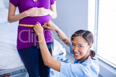 Portrait of doctor measuring pregnant womans belly in ward