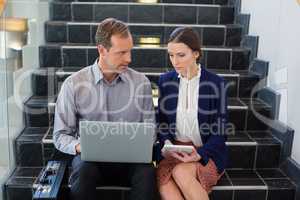 Businessman and woman sitting on steps using laptop