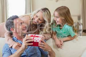 Father receiving a gift from his daughter and wife in living room