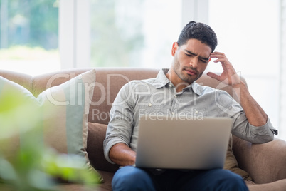 Man sitting on sofa and using laptop in living room at home