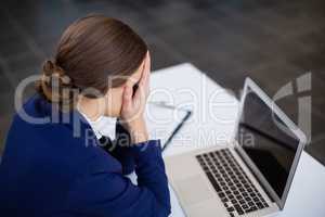 Tired businesswoman sitting at desk with laptop