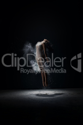 Young girl jumping in white dust cloud in studio