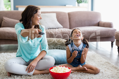 Mother and daughter watching television while having popcorn in living room