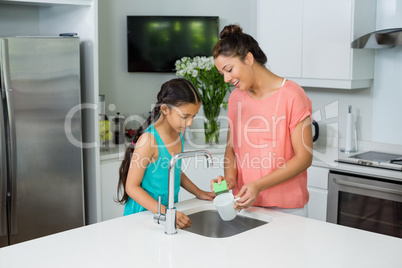 Mother assisting her daughter in cleaning vessel