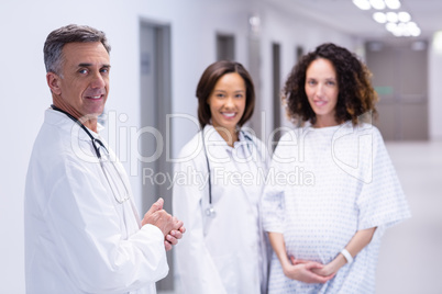 Portrait of pregnant woman and doctors standing in corridor