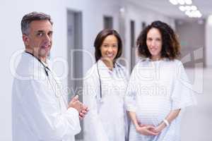 Portrait of pregnant woman and doctors standing in corridor
