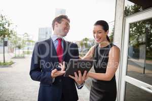 Businessman and colleague discussing over digital tablet and laughing