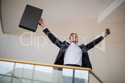 Businessman holding a briefcase and mobile phone cheering