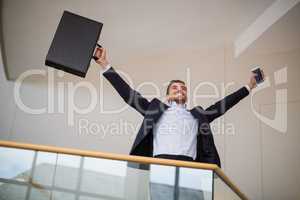 Businessman holding a briefcase and mobile phone cheering