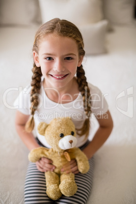 Girl holding a teddy bear on bed in bedroom