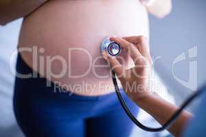 Hands of doctor examining pregnant womans belly with stethoscope