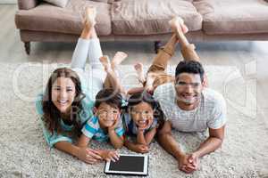 Portrait of parents and children lying on rug and using digital tablet
