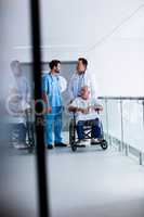 Doctors interacting with each other with patient on wheelchair in passageway
