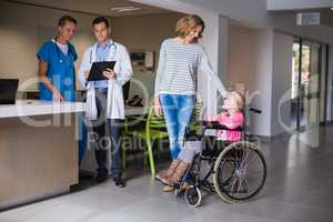 Doctors discussing over clipboard and woman standing with disable girl